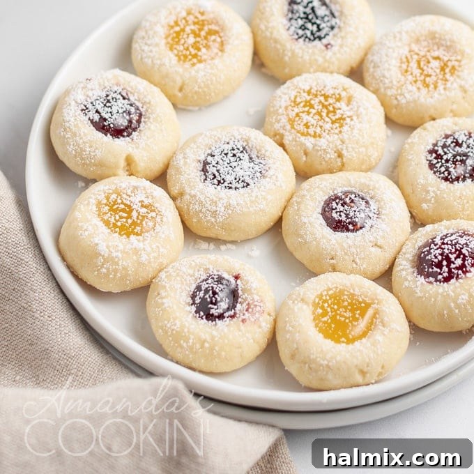 A close-up of delicious thumbprint cookies, perfectly baked with vibrant jam centers, resting on a white plate, ready to be enjoyed.