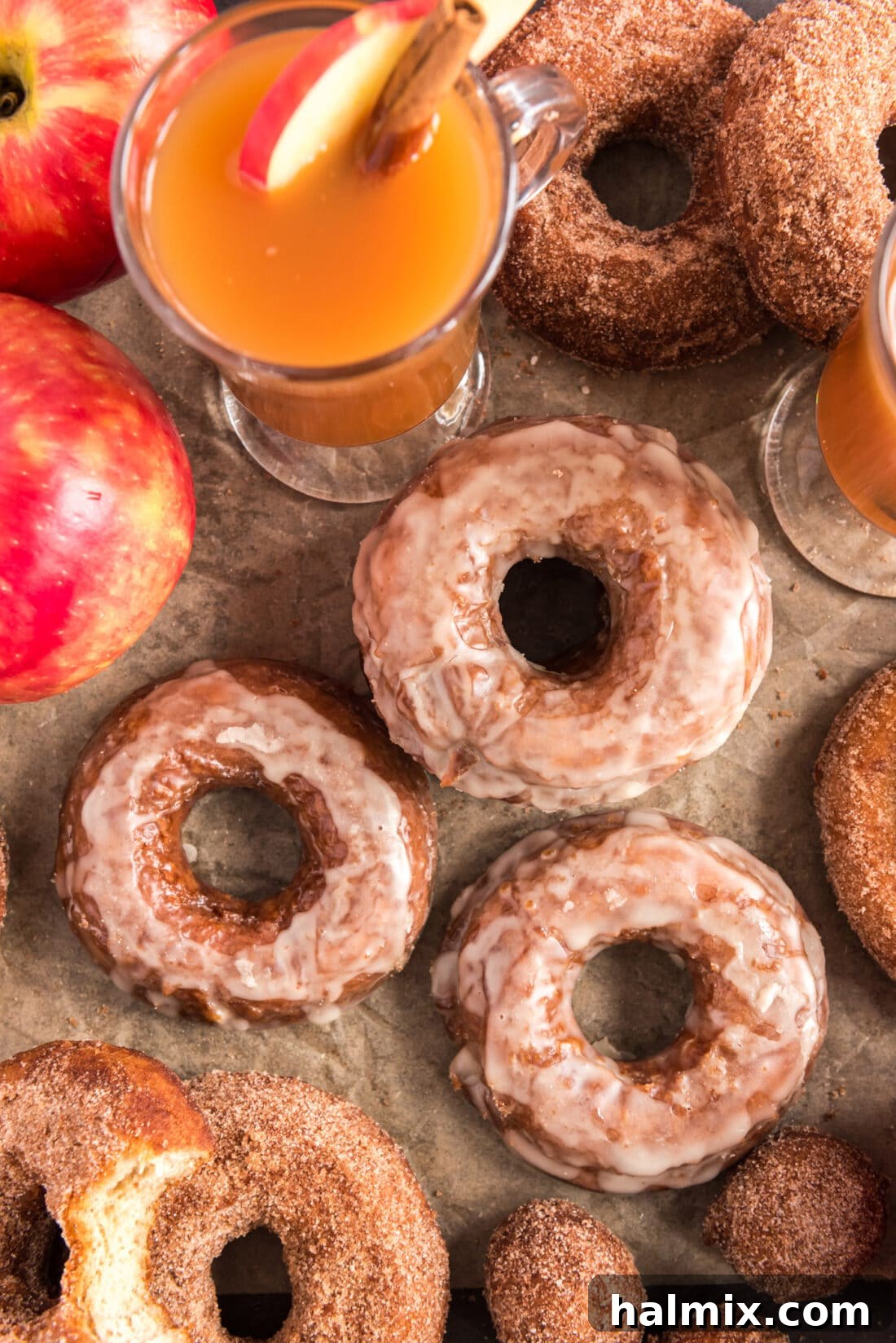 Overhead photo of golden Apple Cider Doughnuts with fresh apples and a jug of apple cider in the background