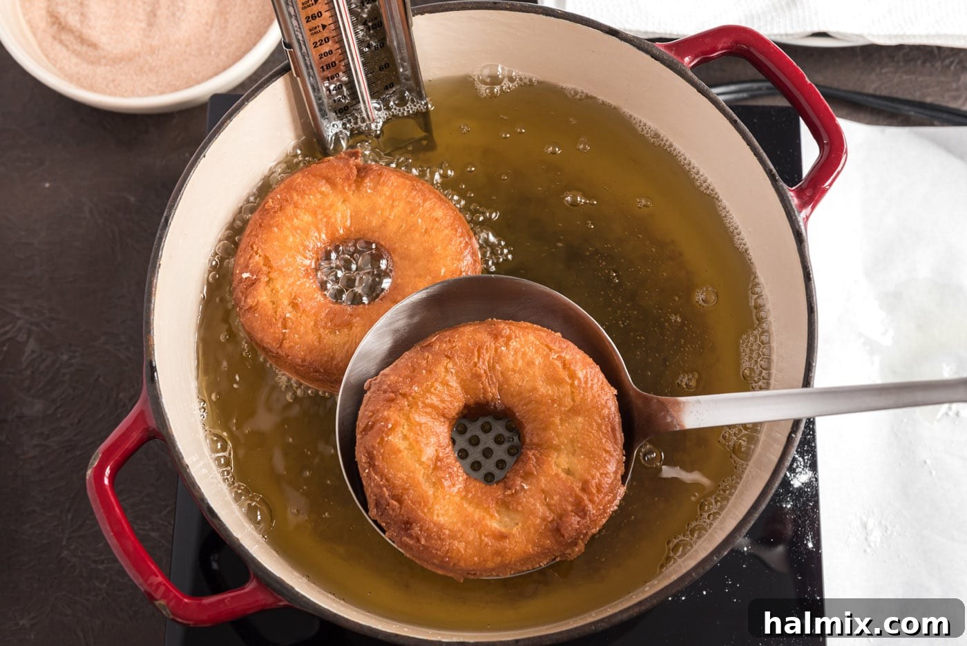 Fried donuts being lifted from hot oil with a slotted spoon to drain