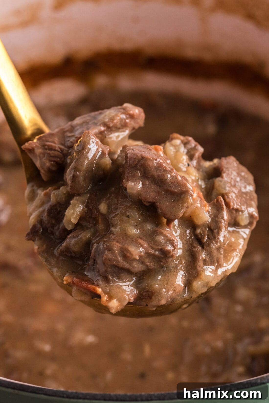 A ladle lifts a generous serving of rich Beef Carbonnade out of a simmering pot, highlighting the tender beef chunks and luscious gravy.