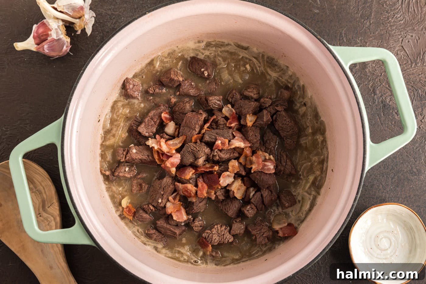 Browned beef and crispy bacon returned to the pot with the simmering onion and beer mixture, ready for slow cooking.