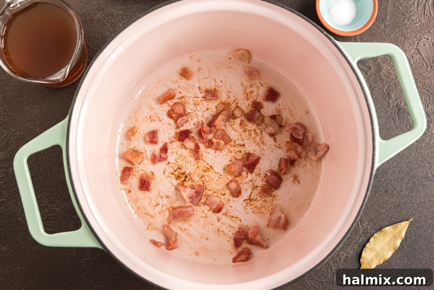 Diced bacon sizzling in a Dutch oven, cooking until crisp and rendering its flavorful fat.