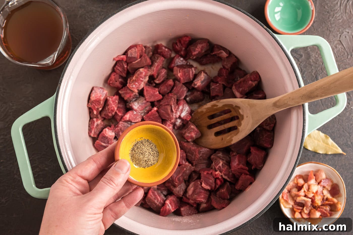 Cubed chuck roast being seasoned with salt and pepper before browning in a Dutch oven, enhancing its flavor.