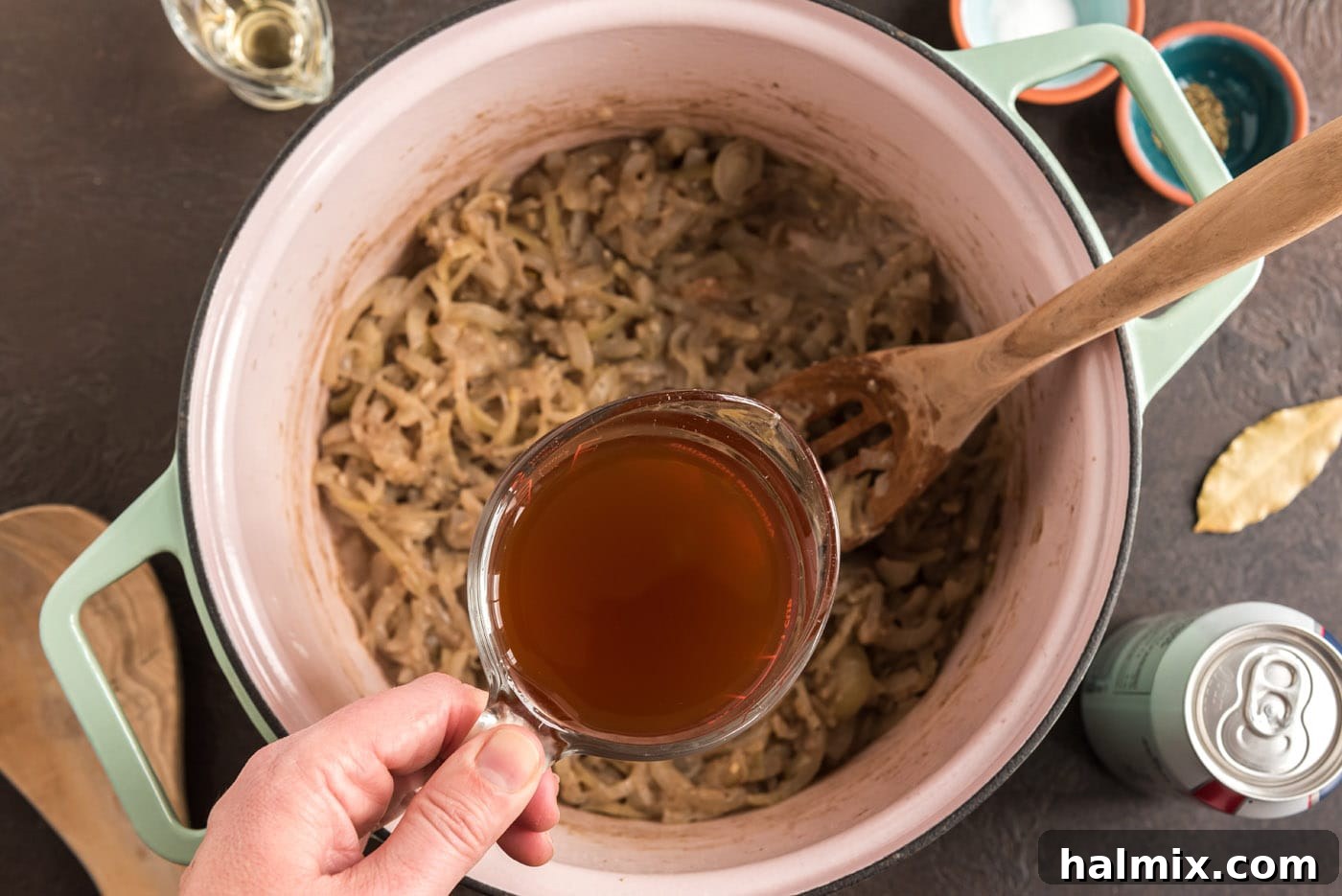 Pouring rich beef broth into the Dutch oven with the onion and flour mixture, adding liquid depth to the Carbonnade.