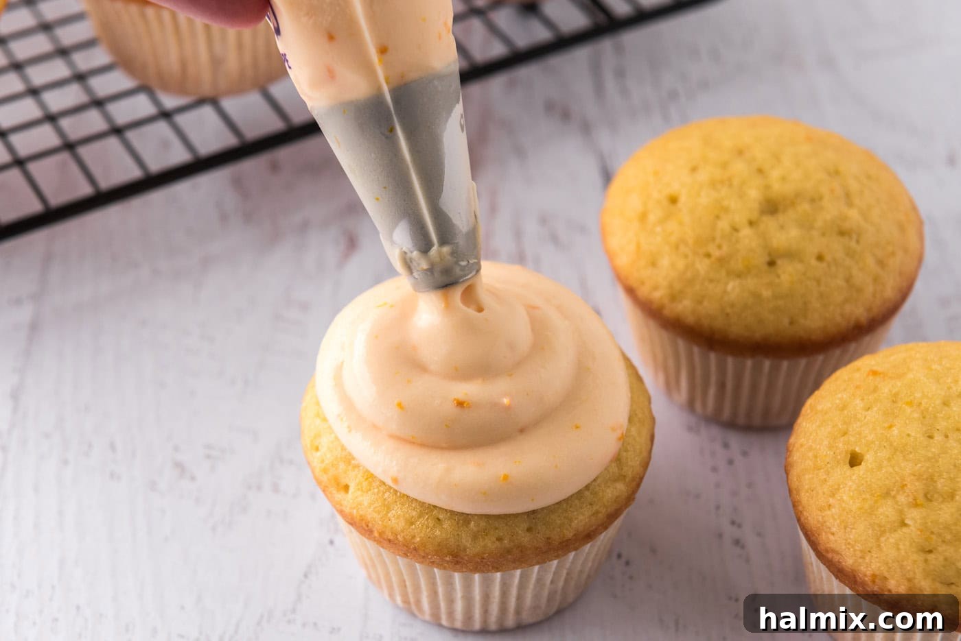 Piping orange creamsicle frosting onto baked cupcakes with a piping bag.