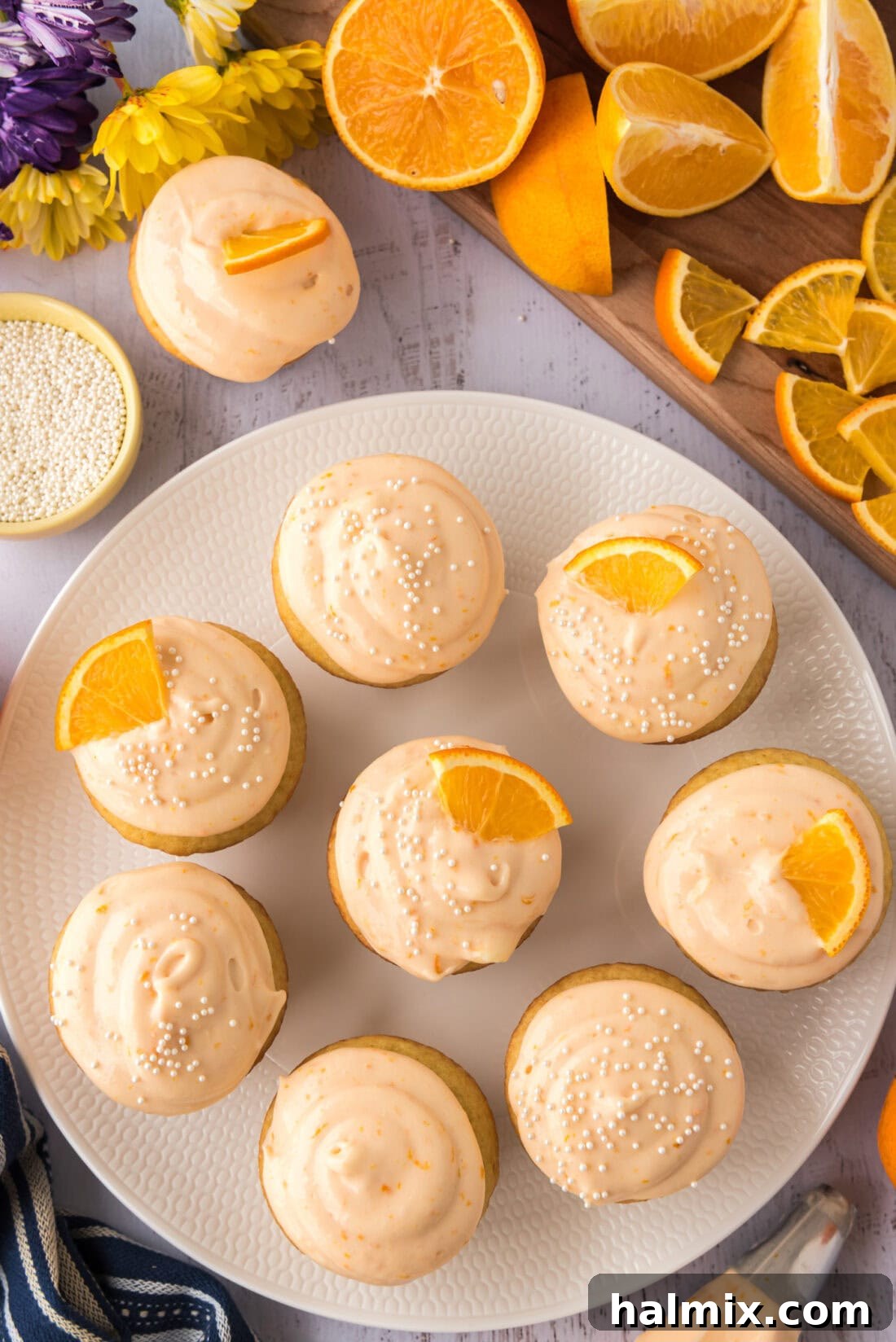 A plate filled with beautifully frosted Orange Creamsicle Cupcakes, garnished with orange wedges and sprinkles.