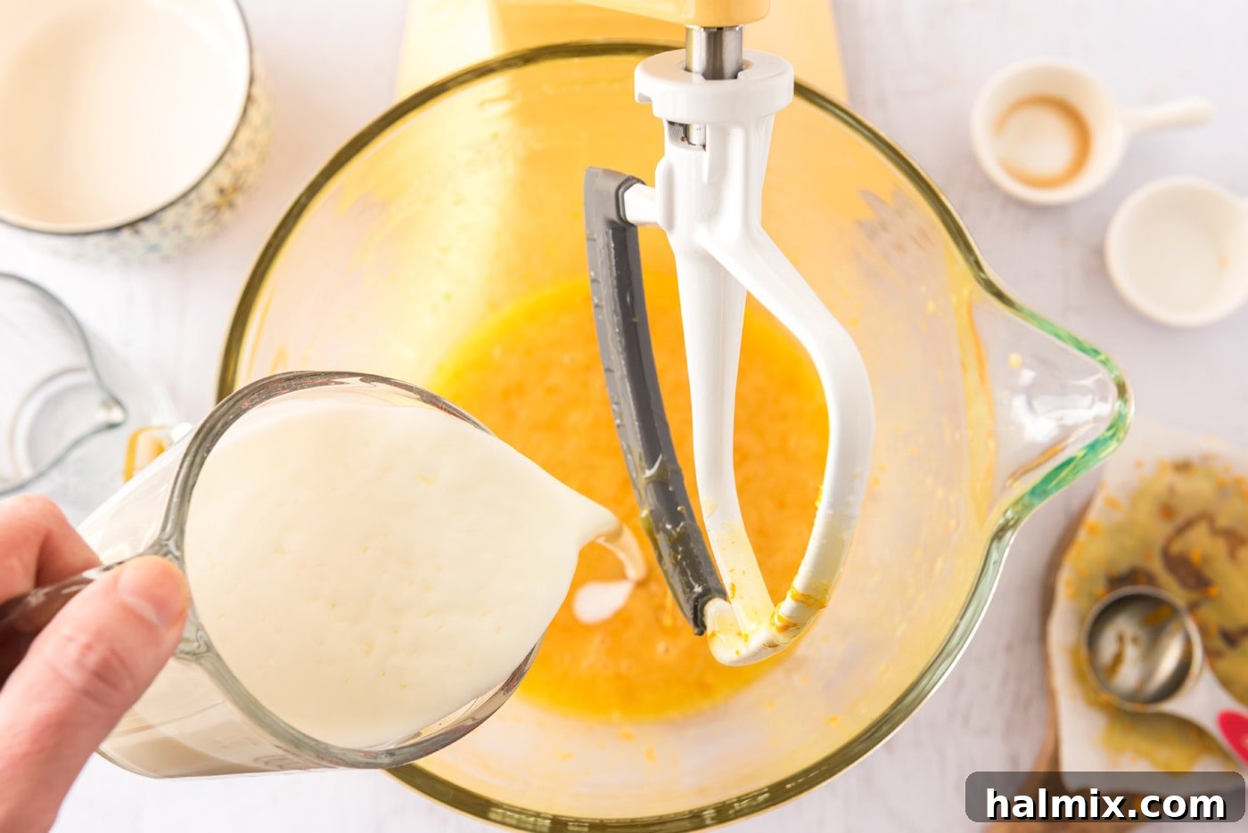Pouring buttermilk into the orange egg mixture in a stand mixer.