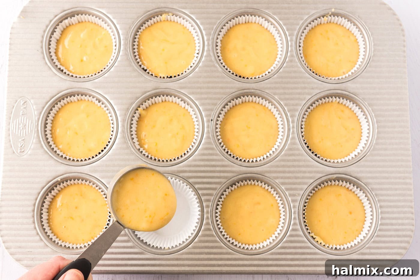 Spoonfuls of orange cupcake batter being spooned into a cupcake pan lined with paper wrappers.
