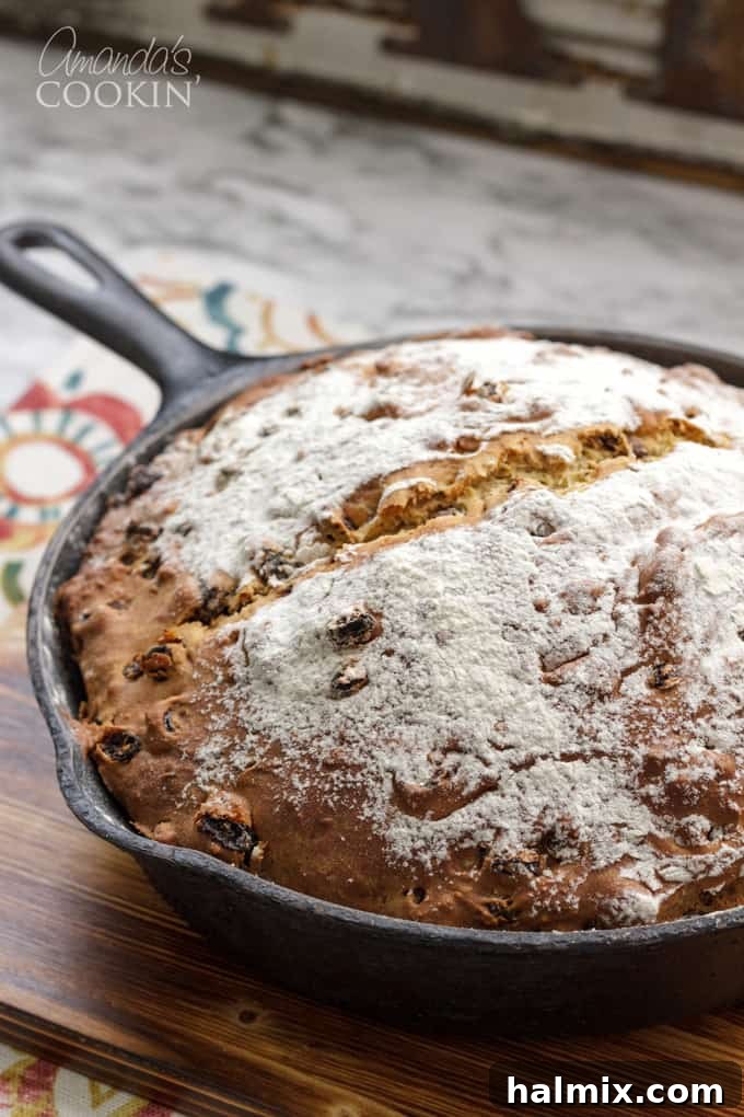 A round loaf of Irish soda bread, baked to a golden brown perfection, rests in a cast iron skillet, ready to be cooled and sliced.