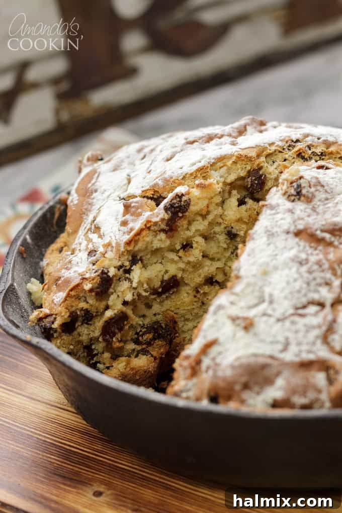 A freshly baked Irish soda bread, with a perfect cross scored on top, has a slice removed to show its inviting texture and raisin-filled interior.