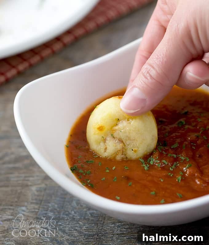 A delicious pepperoni pizza puff being gently dunked into a small white bowl of vibrant red pizza sauce, illustrating the perfect dipping experience.