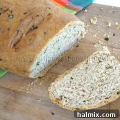 A close up photo of a sliced loaf of scallion chive bread with garlic and rosemary on a wooden cutting board.