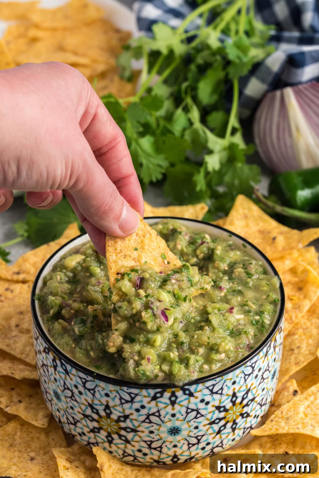 Hand scooping up some vibrant Tomatillo Onion Avocado Salsa with a golden tortilla chip