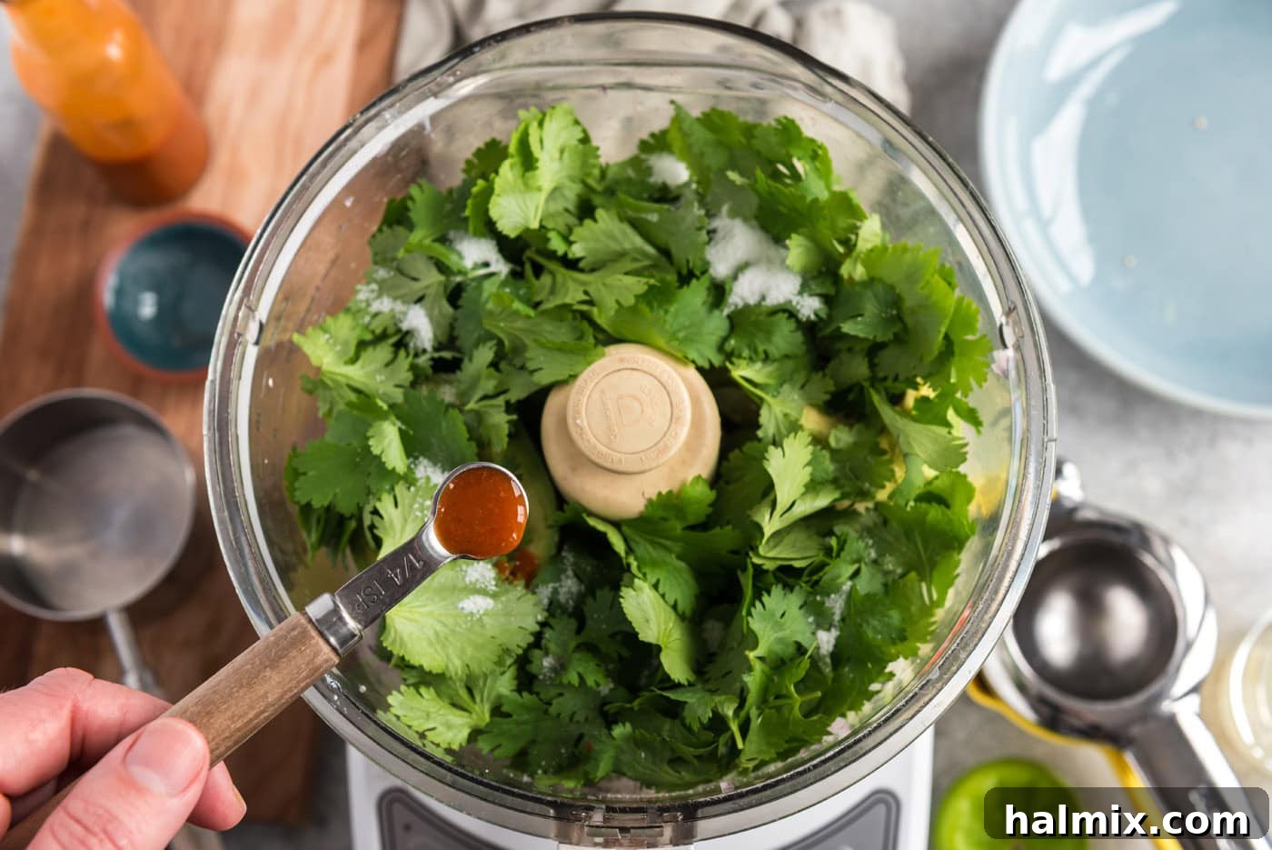 Adding hot pepper sauce to the food processor along with cilantro, onion, avocado, and chile peppers