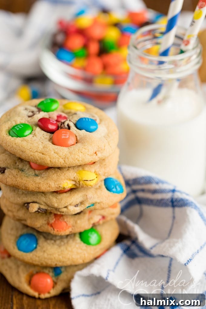 Jumbo Chocolate Chip M&M Cookies are an easy and festive treat. Two jumbo M&M cookies with a glass of milk, inviting a delicious treat.