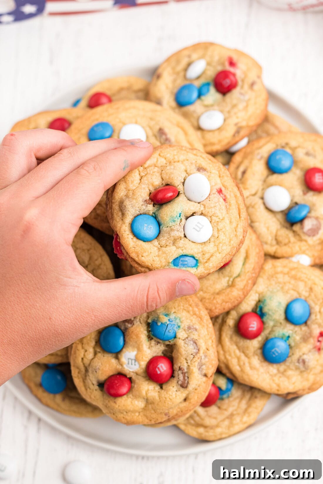 Chewy M&M Chocolate Chip Cookies 2 A child joyfully selecting a red, white, and blue M&M cookie from a plate, highlighting its patriotic appeal.
