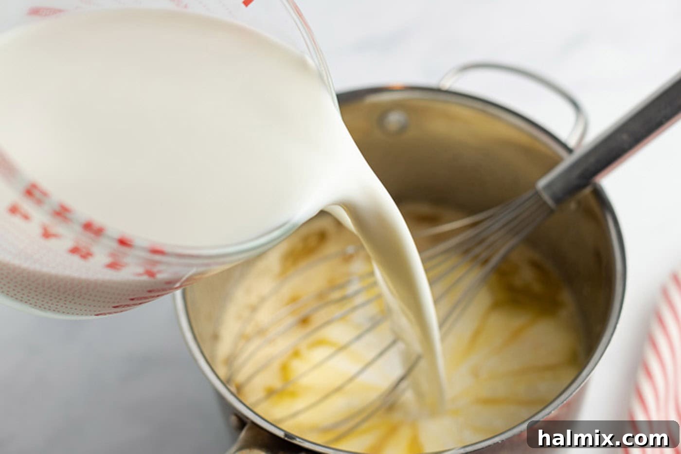 Milk being slowly added to the egg mixture in a saucepan while whisking