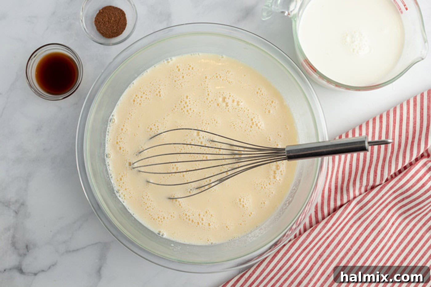 Eggnog mixture in a bowl with vanilla, nutmeg, and milk nearby