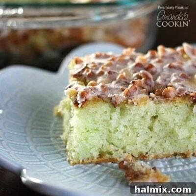 A close up of a slice of pistachio poke cake on a plate, showing its distinctive green color.