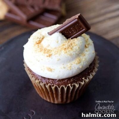 A close up of a s'mores cupcake topped with a Hershey bar piece, showcasing its tempting layers.