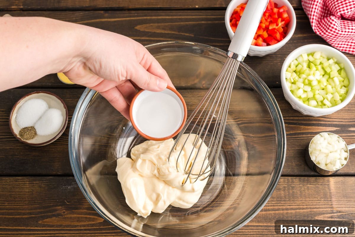 Nana's Classic Macaroni Salad 3 Adding white vinegar to mayonnaise in a large mixing bowl, showcasing the start of the dressing preparation.