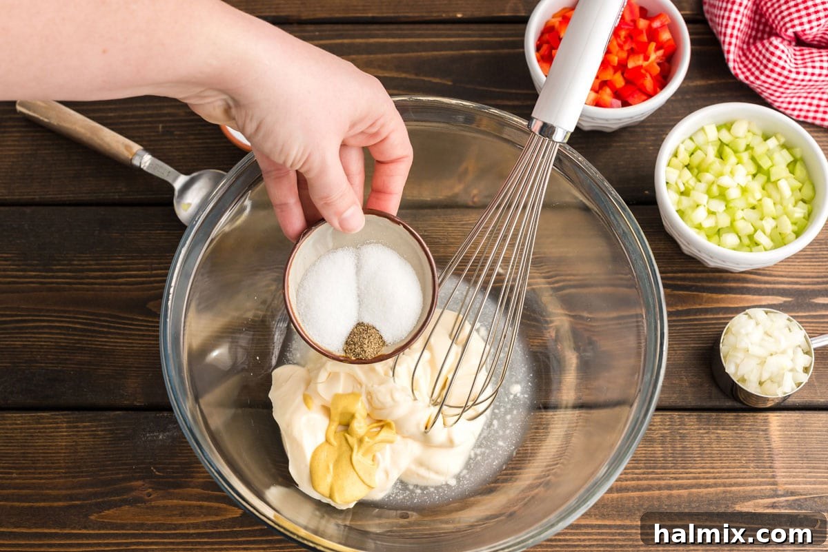 Nana's Classic Macaroni Salad 4 Adding salt and pepper to the mixing bowl containing mayonnaise and mustard, enhancing the dressing's flavor.