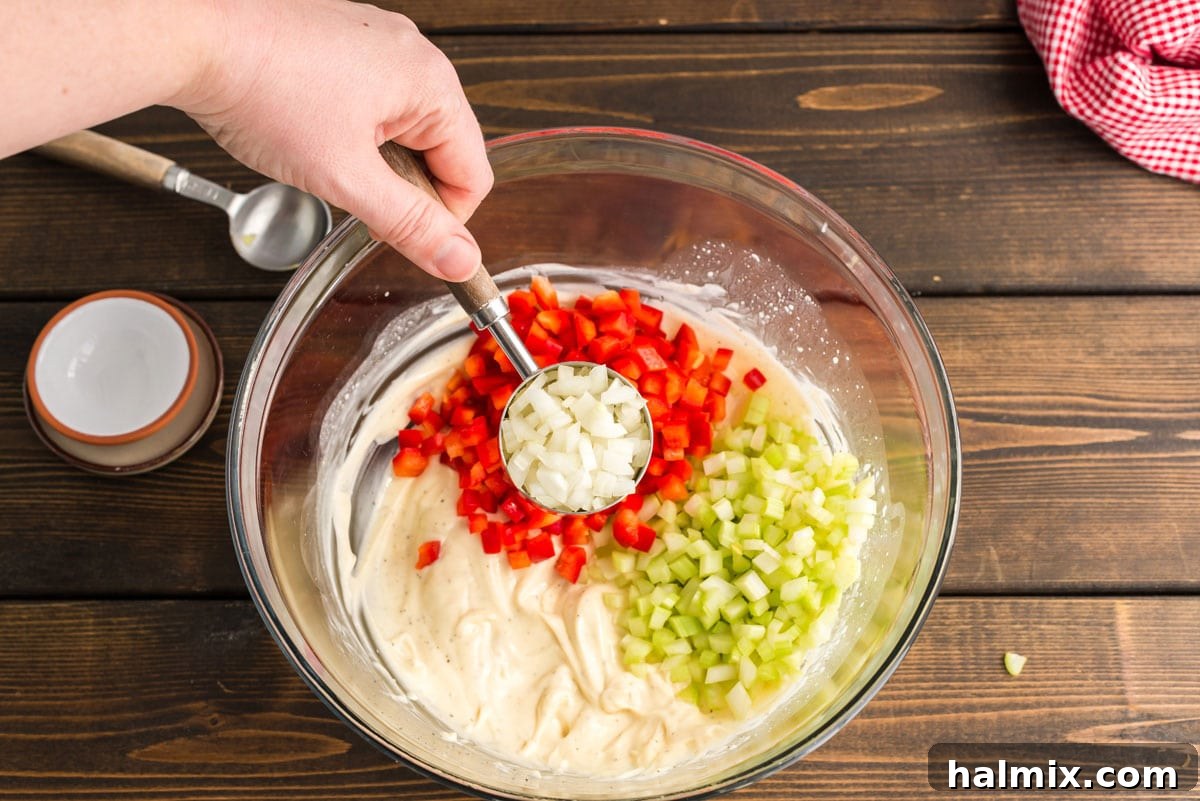 Nana's Classic Macaroni Salad 5 Incorporating diced onion into the creamy dressing and other vegetables in a large bowl, highlighting the combination of flavors.
