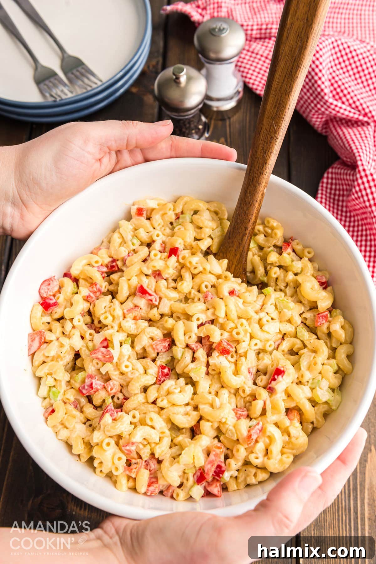 Serving Nana's Macaroni Salad at a Family Gathering Hands carefully placing a white bowl of creamy macaroni salad onto a rustic wooden table, ready for serving.
