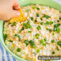 green bowl of corn dip, hand dipping tortilla chip
