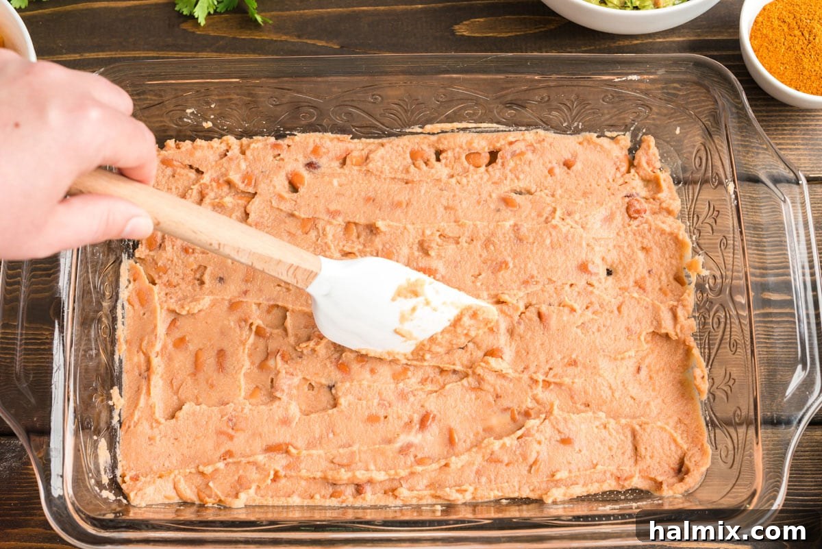 spreading refried beans in a glass pan