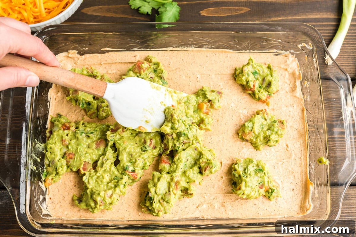 spreading guacamole over sour cream mixture on pan