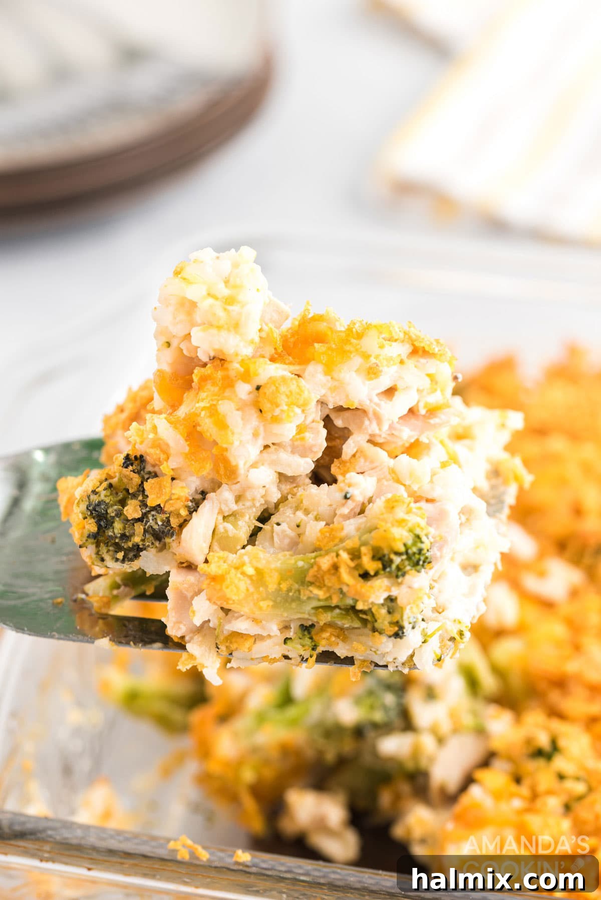 A spatula lifting a portion of hot, bubbling chicken and rice casserole from a baking dish