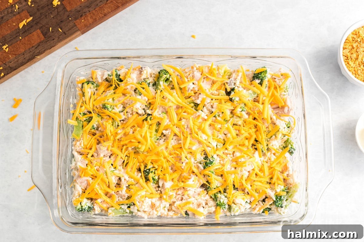 A baking dish filled with chicken and rice casserole mixture, topped with an even layer of grated cheddar cheese