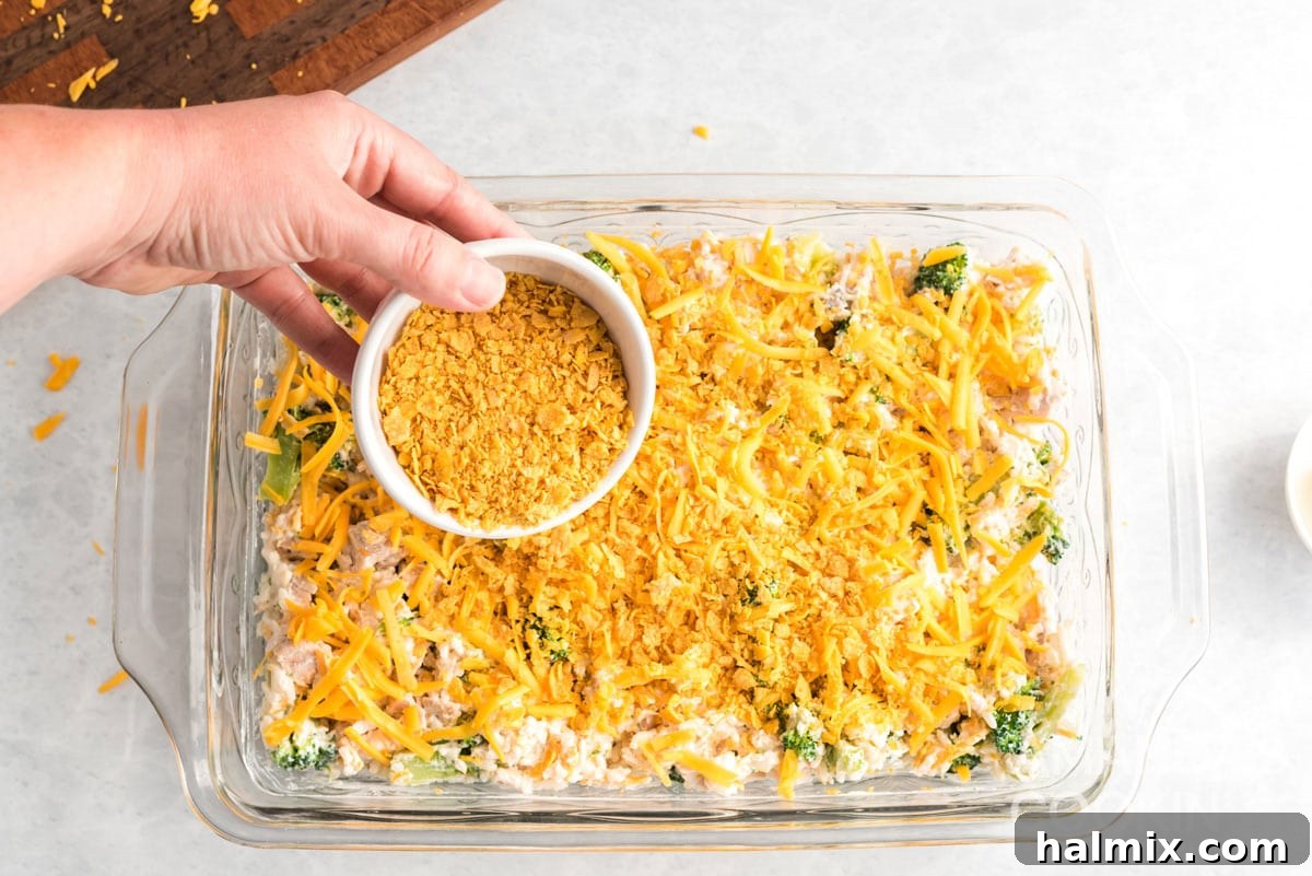 Crushed Corn Flakes being sprinkled over the top of the chicken and rice casserole, followed by a drizzle of melted butter, before baking