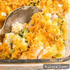 Close up of a spoon scooping a portion of Chicken Broccoli Rice Casserole, showing the creamy texture and crispy topping