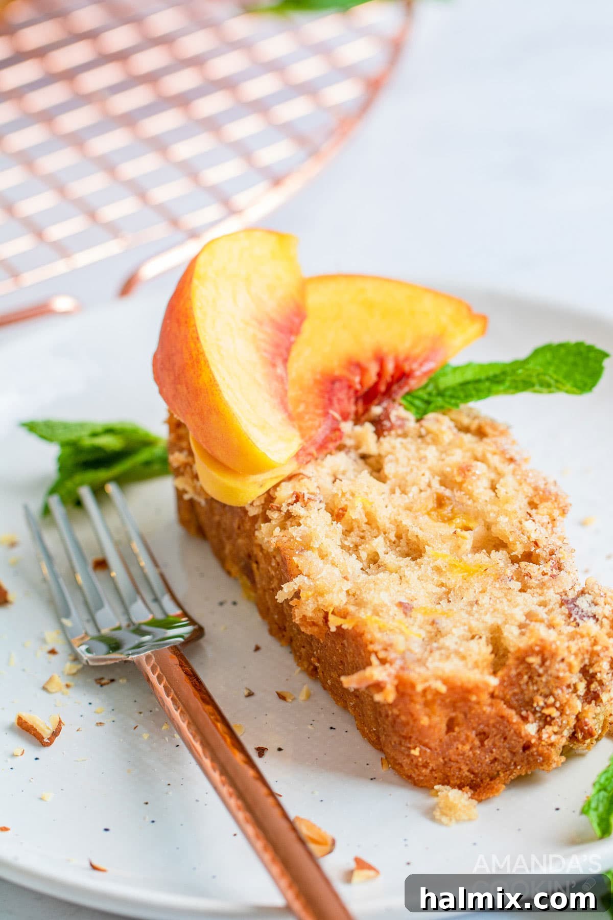 The delicious peach bread is studded with almonds and topped with an amazing cinnamon almond mixture you will love. A perfectly baked slice of peach bread, studded with almonds, rests on a plate beside a fork, ready to be enjoyed.