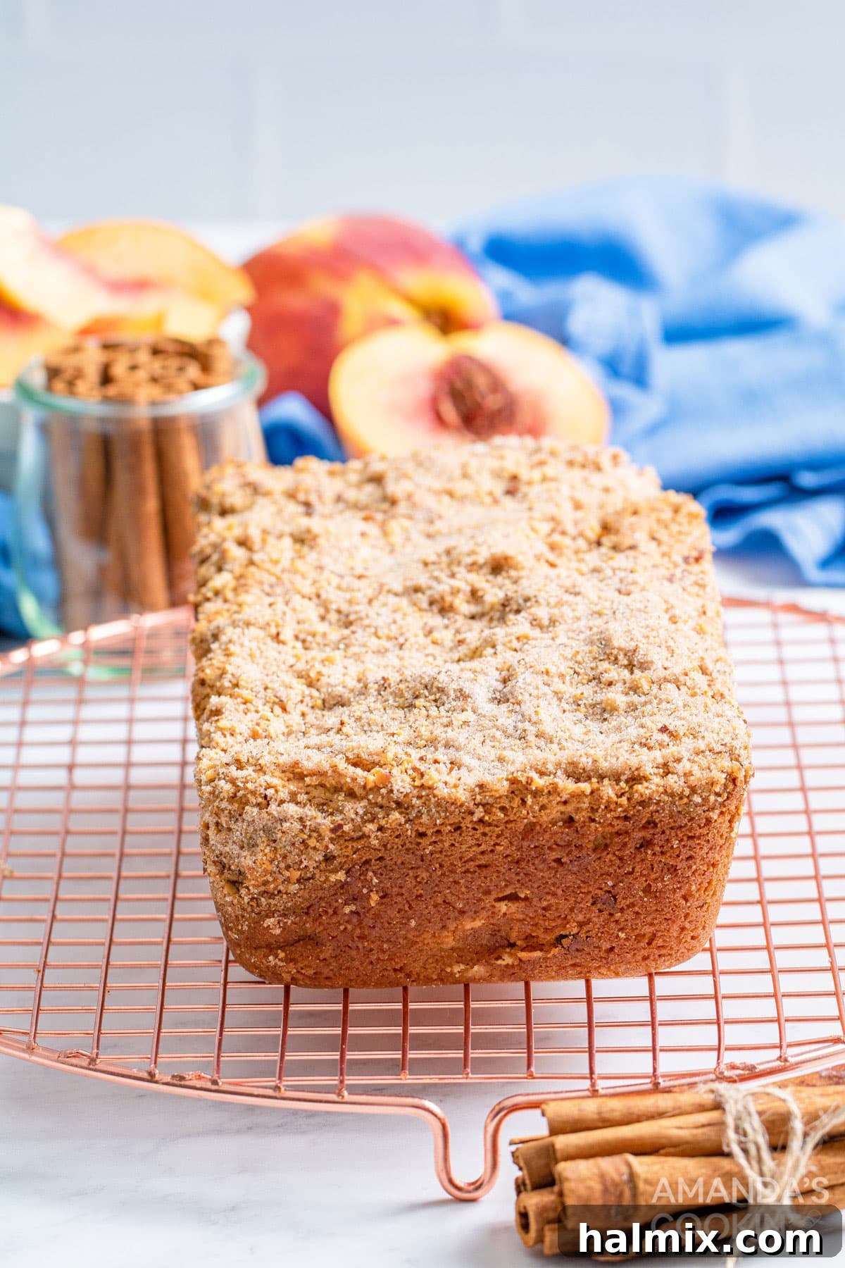 The delicious peach bread is studded with almonds and topped with an amazing cinnamon almond mixture you will love. A warm, golden-brown loaf of peach bread, still in its pan, rests on a wire cooling rack, emitting a delightful aroma.