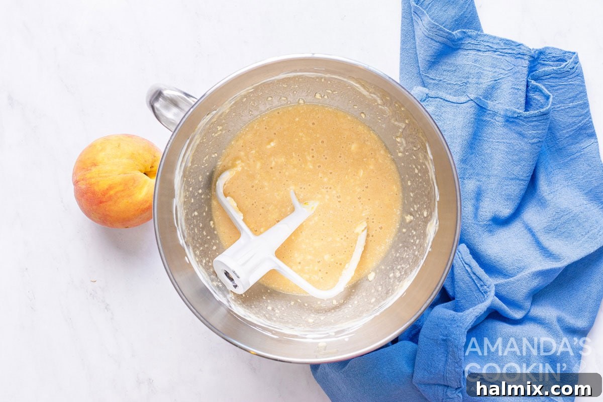 Golden Peach Loaf 3 A bowl of creamy, blended wet ingredients for peach bread, mixed with a paddle attachment.