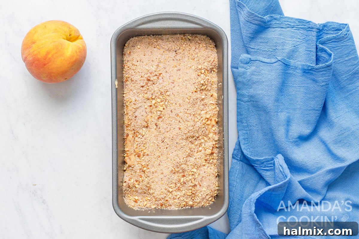 Golden Peach Loaf 6 Peach bread batter scooped into a loaf pan, generously topped with a cinnamon almond mixture, ready for baking.