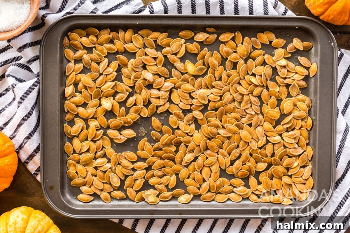 A baking pan filled with golden-brown, freshly roasted pumpkin seeds, sparkling with salt.