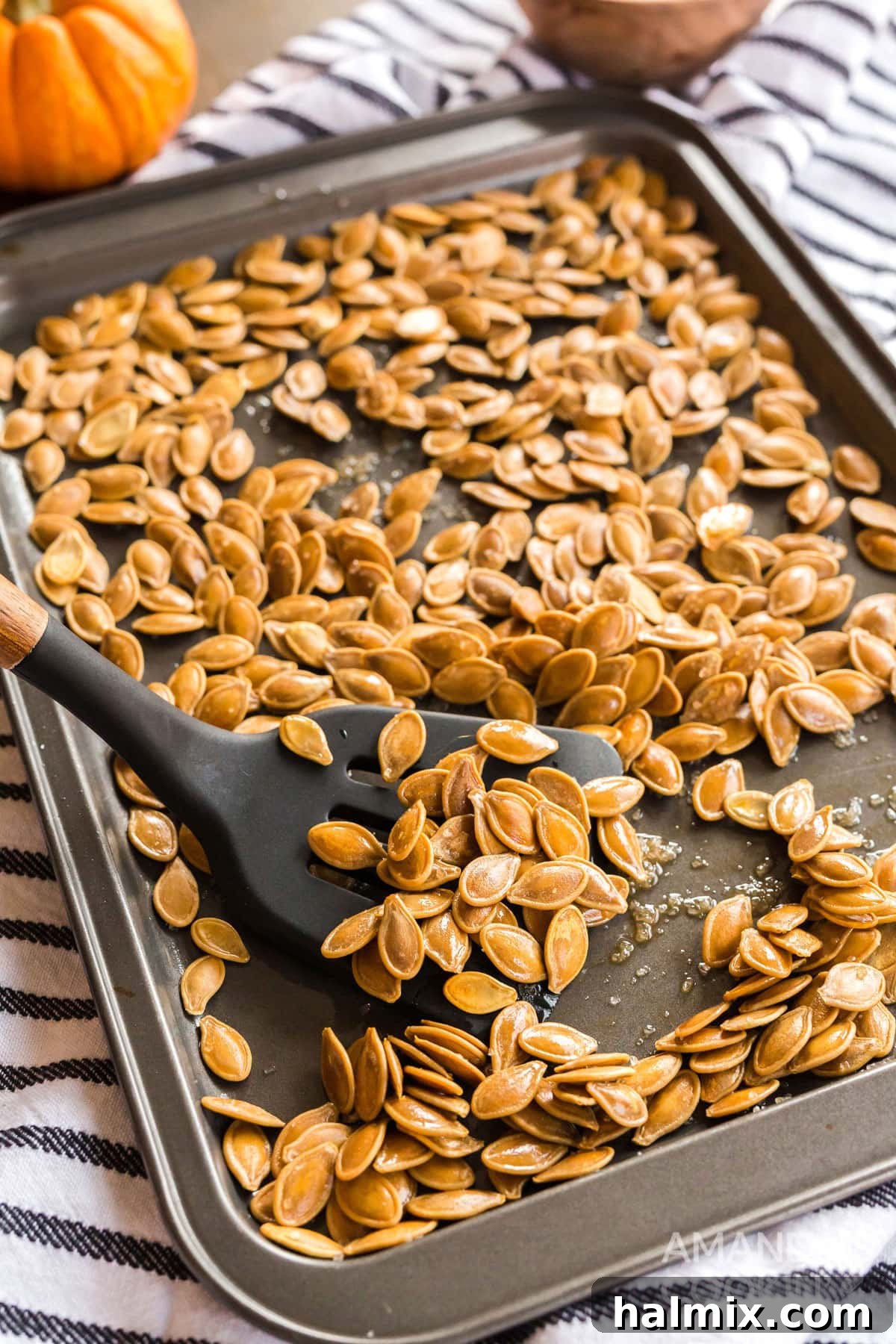A baking sheet laden with golden, crispy roasted pumpkin seeds, alongside a spatula ready to serve.