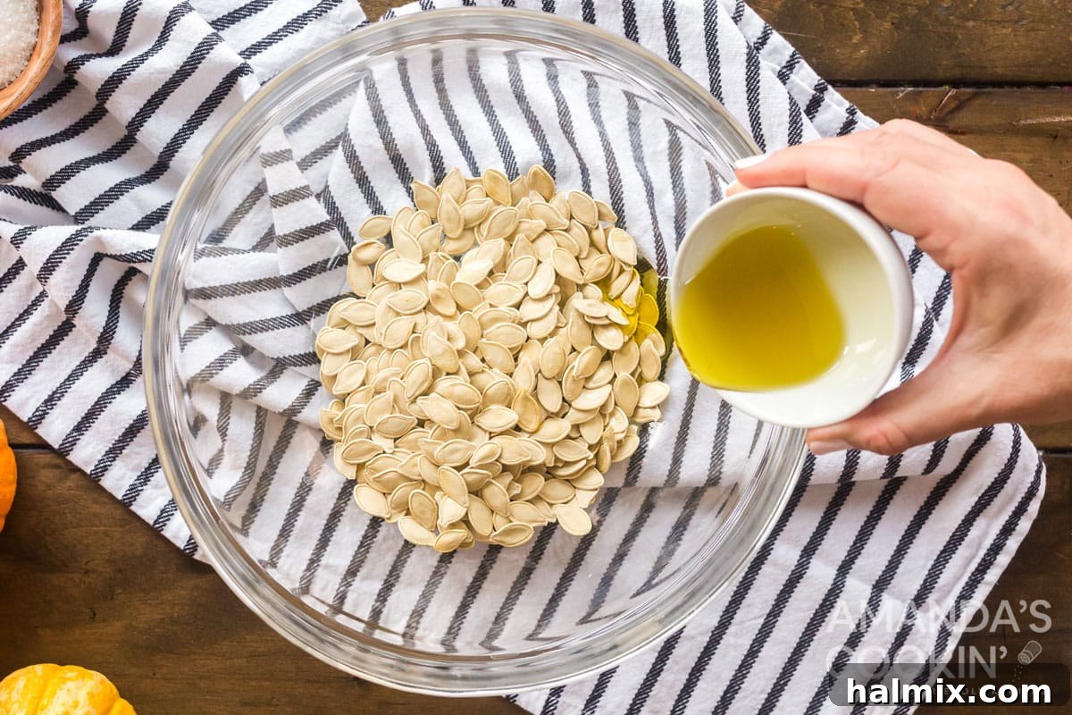 Adding olive oil to pumpkin seeds in a mixing bowl, preparing them for roasting.