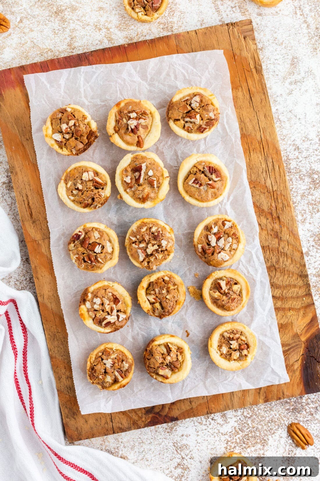 A collection of golden-brown pecan tassies perfectly arranged on a rustic cutting board.