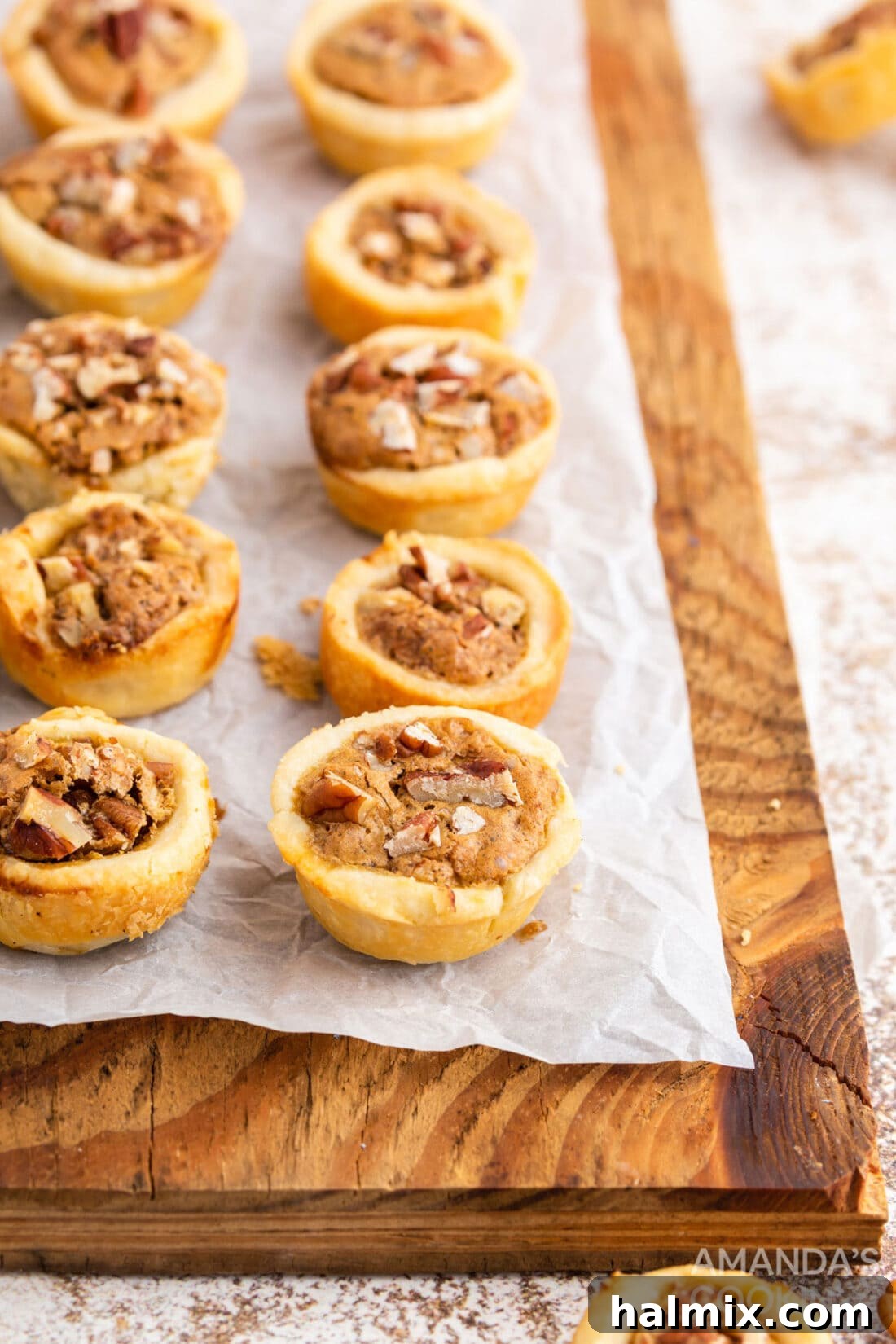 Freshly baked pecan tassies cooling on a rustic wood cutting board, showcasing their golden-brown crust and rich filling.