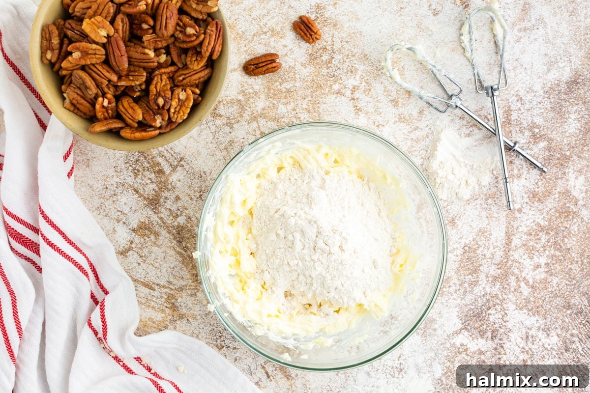 Mixing flour into the butter and cream cheese dough in a bowl, showing the consistency as it begins to form a ball.