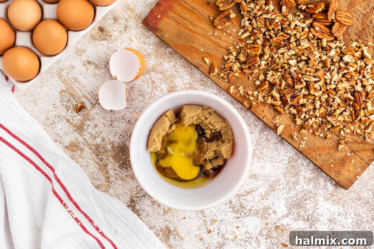 Bowl with an egg, brown sugar, and extracts, ready to be whisked for the pecan tassie filling.