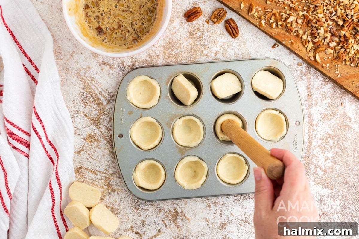 Pressing dough into the mini muffin tin cavities to form the tassie crusts.