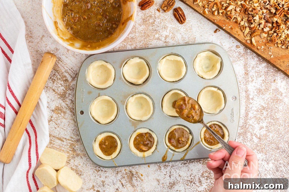 Spoonfuls of pecan filling being placed into the dough-lined mini muffin tin cups.
