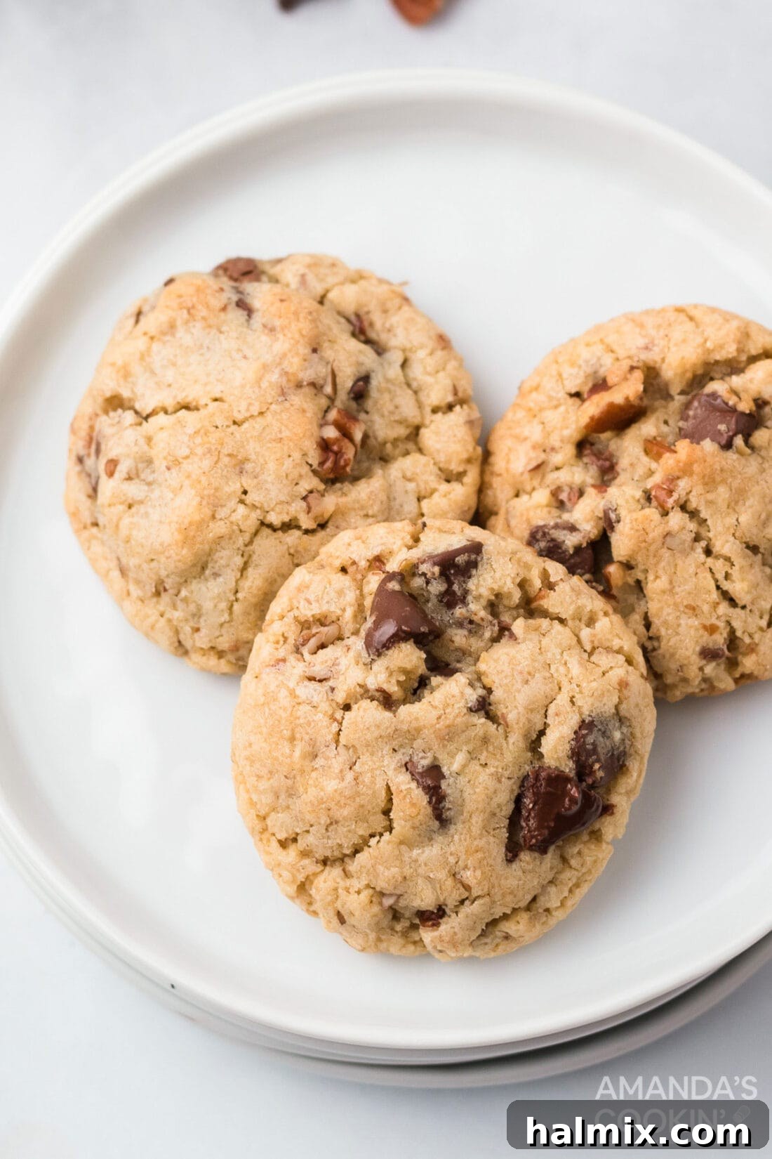 A plate overflowing with golden-brown Neiman Marcus cookies, studded with melted chocolate and nuts.