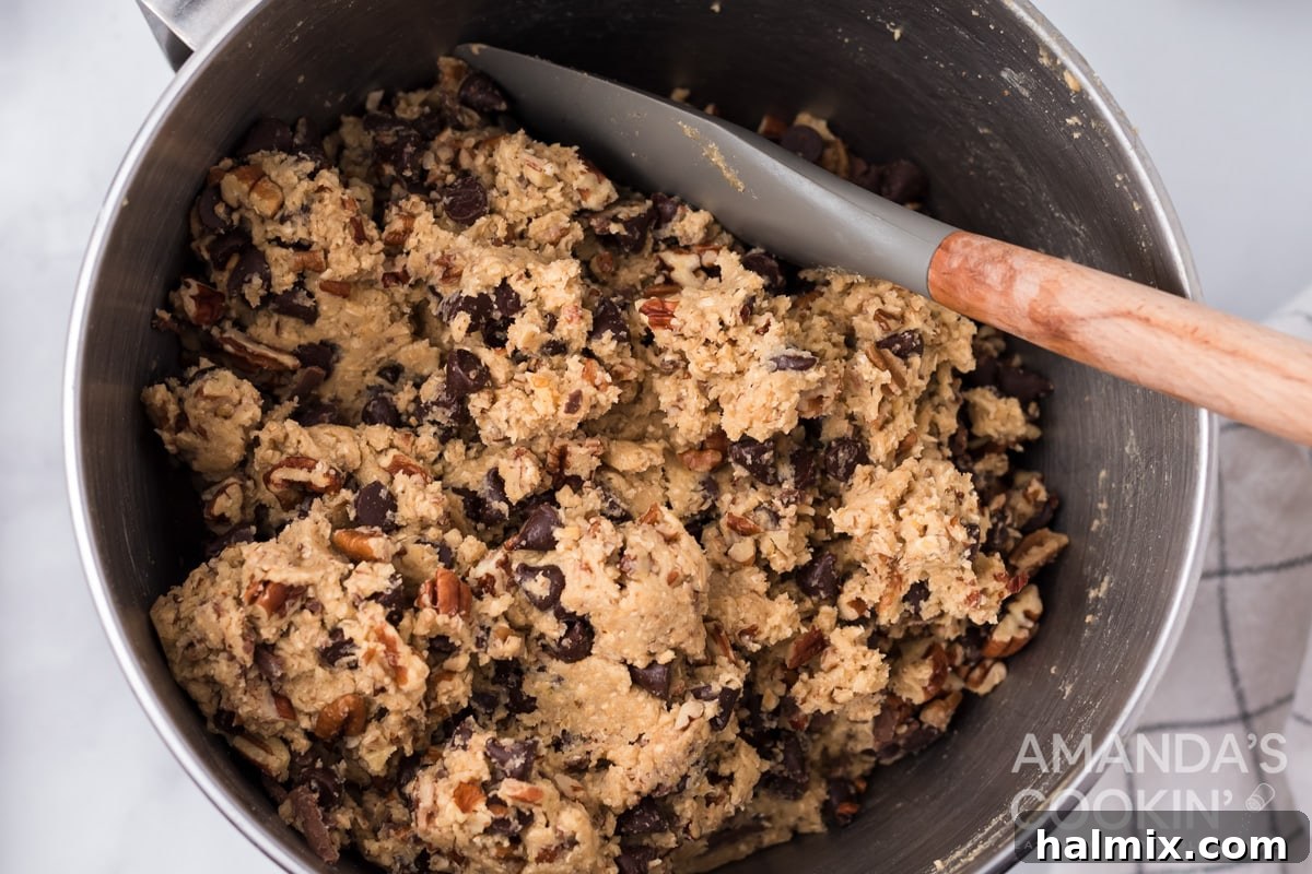 Thick cookie dough in a bowl with chocolate chips, grated chocolate, and nuts mixed in.